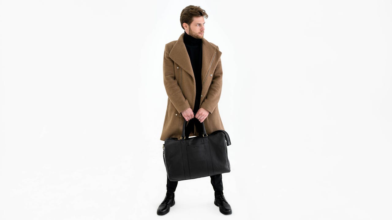 services-05 Fashionable man in coat holding a duffel bag in a minimalist studio setting.